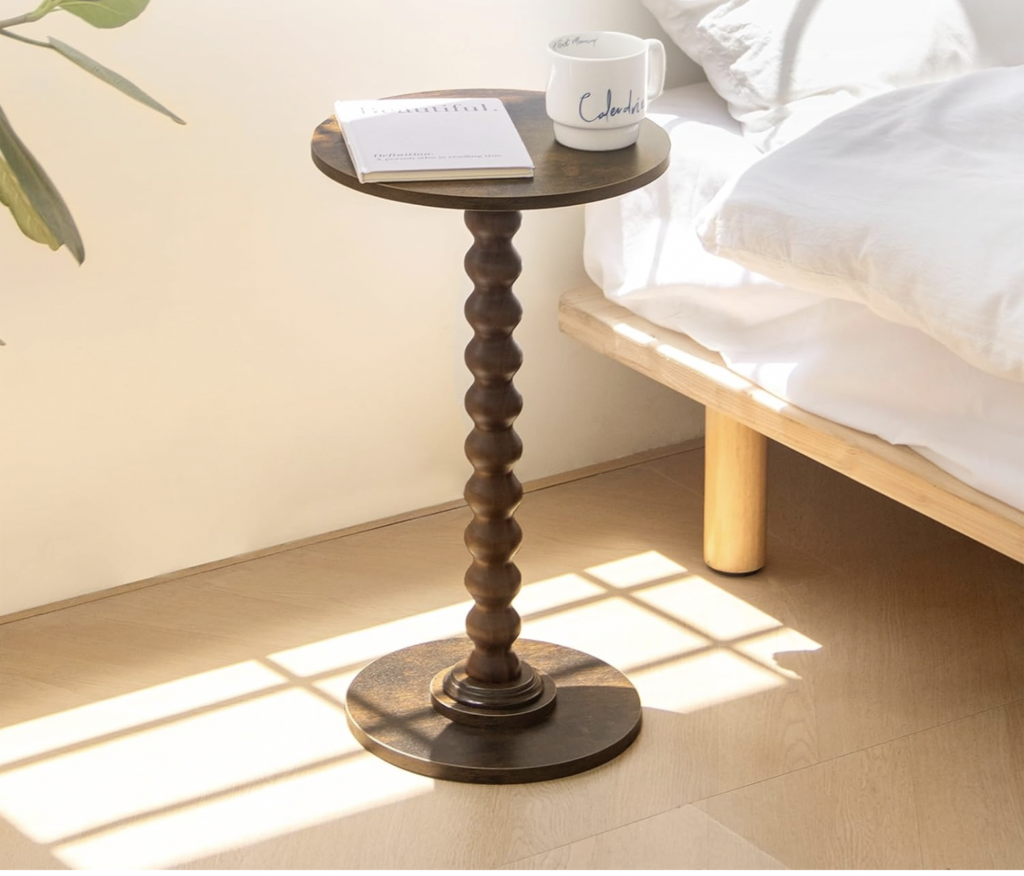 a beautiful tall round pedestal table styled next to a bed
